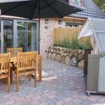 Terrace with wooden table, chairs, and umbrella. Backyard with stone wall and garden.