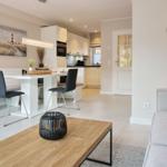 Living and dining area with kitchenette and sofa. Wooden table, gray seating, and wall art.