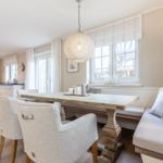 Dining area with wooden table, bench, and chairs. Kitchen area in background.