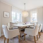 Dining room with table, chairs, and windows. Ceiling light and wooden floor.