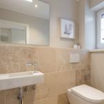 Bathroom with sink, mirror, and toilet. Window with shell decoration.