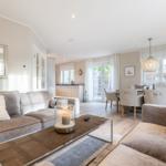 Living and dining area with sofa, table and chairs. Windows with curtains and ceiling light.