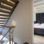 Treppenhaus mit Holzstufen und Glasgeländer. Blick in Schlafzimmer mit Bett und Vorhang.