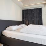 Schlafzimmer mit Bett, weißen Laken und dunklen Vorhängen.