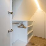 Kleiderschrank mit Haken und Regalen unter schräger Decke.