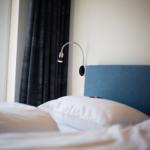 Bettkopfteil mit blauer Polsterung, Nachttischlampe und Fenster mit dunklen Vorhängen.