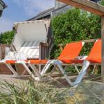 Terrasse mit orangefarbenen Liegestühlen und Sonnenschirm. Holzgeländer und Grünflächen im Hintergrund.