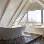 Freistehende Badewanne unter Dachschrägen mit großem Fensterblick auf Landschaft