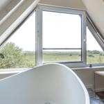 Badewanne mit Blick auf grünes Feld durch Dachfenster