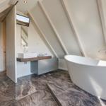 Badezimmer mit freistehender Badewanne, Waschbecken und Toilette unter Dachschrägen.