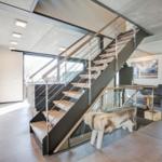 Moderne Wohnung mit Holzstufen und Glasgeländer. Küche, Wohnbereich und Fenster sichtbar.