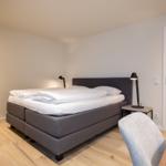 Schlafzimmer mit Bett, Nachttisch und Lampe. Durchgang zu einem Schrankraum.