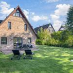 Haus mit Garten, Liegestühlen und Terrasse unter blauem Himmel.