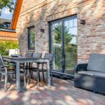 Terrasse mit Tisch, Stühlen und Sofa vor Backsteinhaus.