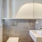 Badezimmer mit Waschbecken, Toilette und Fenster mit Jalousie.