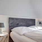Schlafzimmer mit Bett, grauem Kopfteil und zwei Nachttischen mit Lampen.
