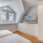 Zimmer mit Dachschrägen, Fenster mit Jalousien, TV und weißer Kleiderschrank.