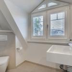 Badezimmer mit Toilette, Waschbecken und Fenster mit Jalousien.