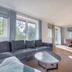 Wohn- und Essbereich mit grauem Sofa, Holzboden und großen Fenstern.