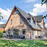 Ferienhaus mit Backsteinfassade, Terrasse und Garten unter blauem Himmel.