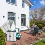 Weiße Villa mit Terrasse, Gartenmöbeln und grüner Umgebung.