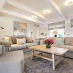 Wohnzimmer mit zwei Sofas, Holztisch und Blumen. Deckenbalken und Fenster mit Jalousien.