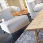 Ein Sessel mit gemusterter Bezugsstoff und schwarzen Beinen steht neben einem Holztisch.