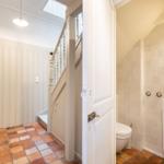 Badezimmer mit Toilette und Waschbecken. Flur mit Treppe und Terrakottboden.