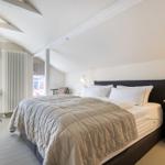 Schlafzimmer mit Bett, Nachttisch und Fenster. Holzdecke mit Balken.