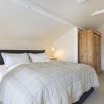 Schlafzimmer mit Bett, Nachttischen und Holzschrank unter schrägen Decken.