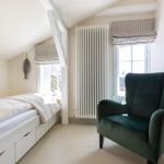 Schlafzimmer mit Bett, grüner Sessel und Fenster mit Rollladen.