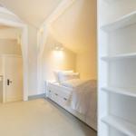 Schlafzimmer mit Dachschrägen, weißem Bett und integriertem Schrank.