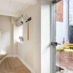 Hallway with wooden floor and stairs. Glass door leads to terrace with table and chairs.