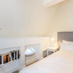 Bedroom with bed, nightstand, bookshelf, and seating nook under sloped ceiling.