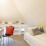 Bedroom with bed, desk, and wall shelf under sloped ceiling.