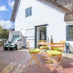 House with terrace, table, chairs, and beach chair. Thatched roof and white walls.