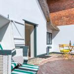 Outdoor area with beach chair, table and chairs in front of white house wall with roof