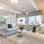 Living and dining area with white sofas, wooden floor, and windows with blinds.