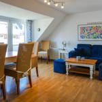 Living and dining area with blue sofa, wooden table, and wicker chairs.