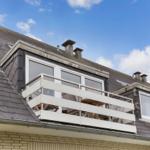 Attic with balcony and large windows under blue sky.