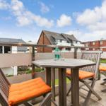 Terrace with wooden table and three chairs with orange cushions.