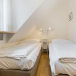 Two single beds under sloped ceiling with window and nightstand.