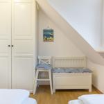 Room with sloped ceiling, wardrobe, chair, and bench with cushions.
