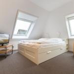 Bedroom with sloped ceiling, bed, TV, and two windows.