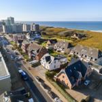 Aerial view of coastal town with houses, streets, and ocean in background.