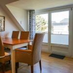 Dining area with table and chairs, view to balcony through windows.