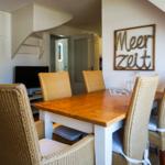 Dining room with wooden table, rattan chairs, and wall art Meer Zeit