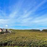 Haus mit Schindeldach auf grüner Hügellandschaft unter blauem Himmel.