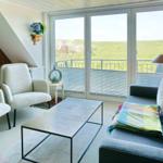 Wohnzimmer mit Sofa, Sessel und Tisch. Balkon mit Blick auf grüne Hügel.