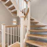 Holzgetriebene Treppe mit weißem Geländer führt zu einer oberen Etage.